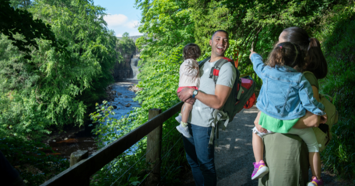family of four stood smiling at each other with High Force Waterfall in the background